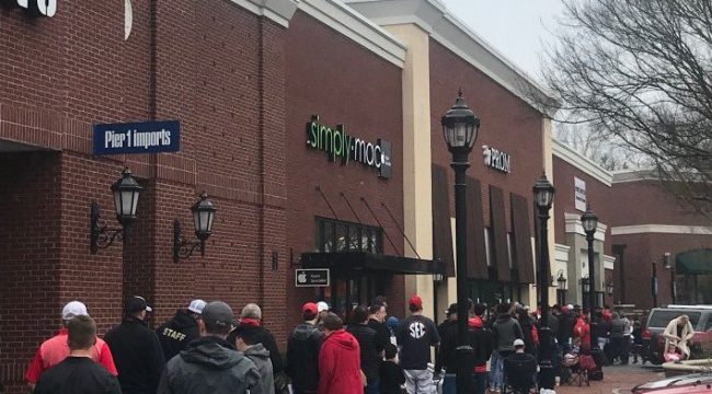 People standing outside in a line outside various store fronts