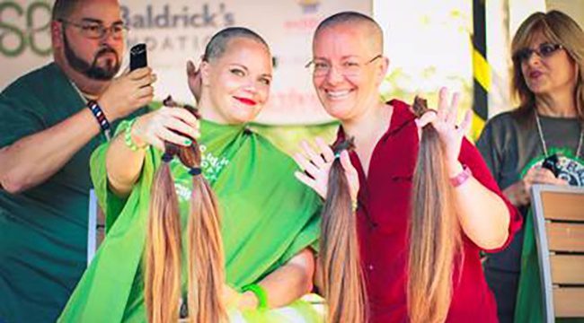 Two woman holding up hair they just shaved and are donating